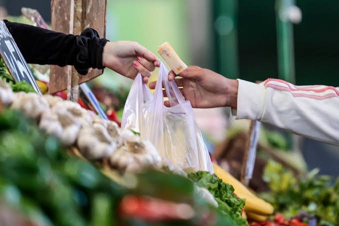 Una persona paga con un billete una compra de verduras en un puesto